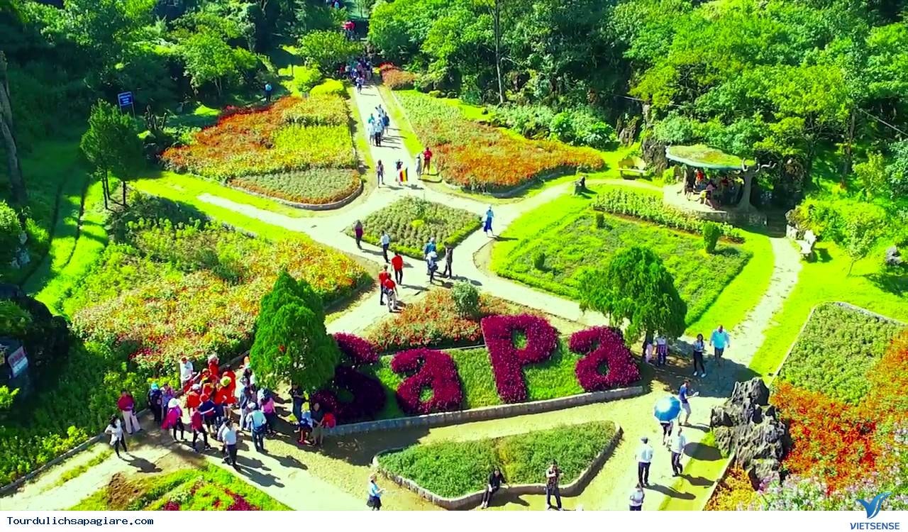 The landscaping is immaculate, with winding paths, neatly trimmed hedges, and flower beds arranged around a green sculpture spelling out “SAPA”
